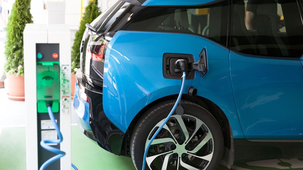 Blue electric vehicle being charged at a public charging station with a blue charging cable connected to the port on the rear side of the car