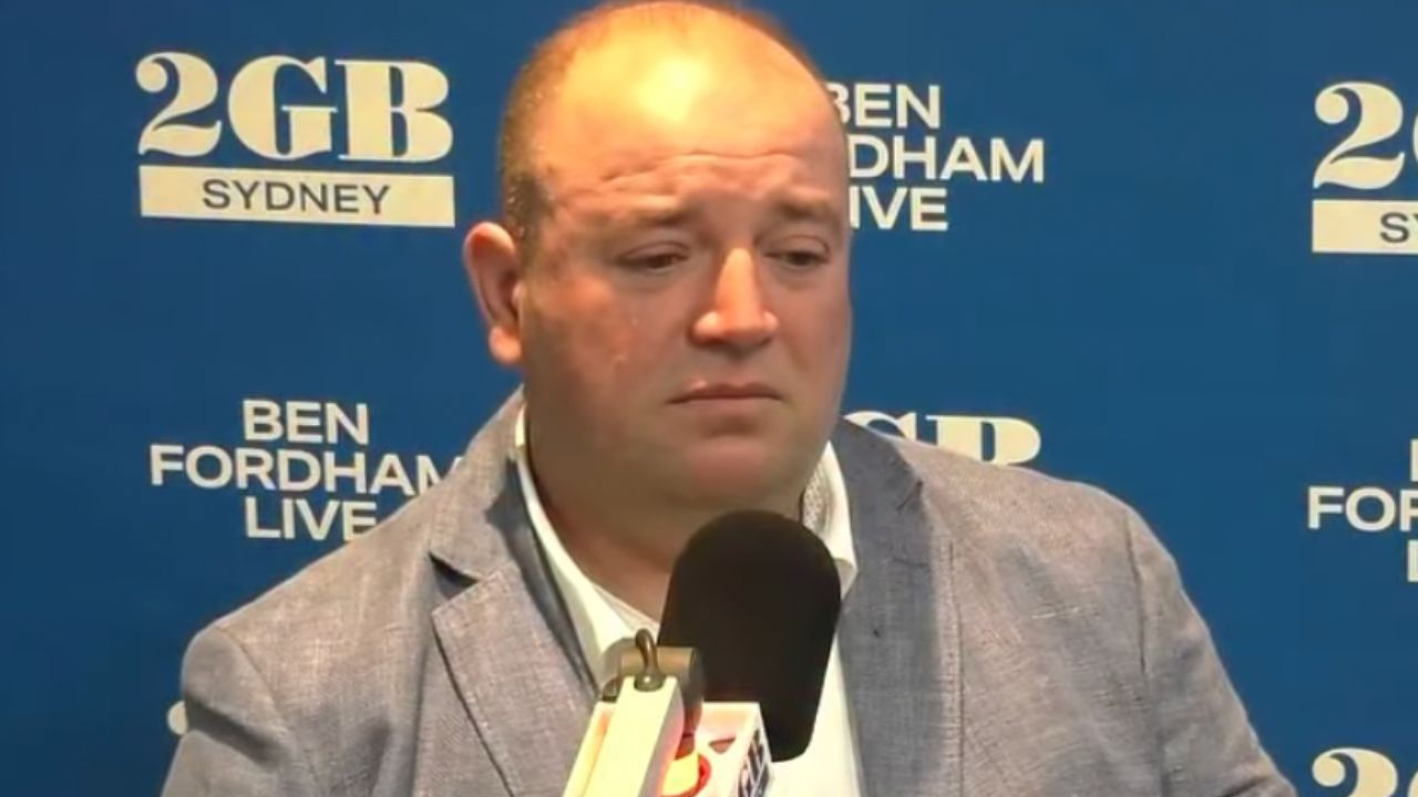 Man in a light gray blazer speaks into a microphone during a televised interview against a blue backdrop that reads 'Ben Fordham Live' and '2GB Sydney'.