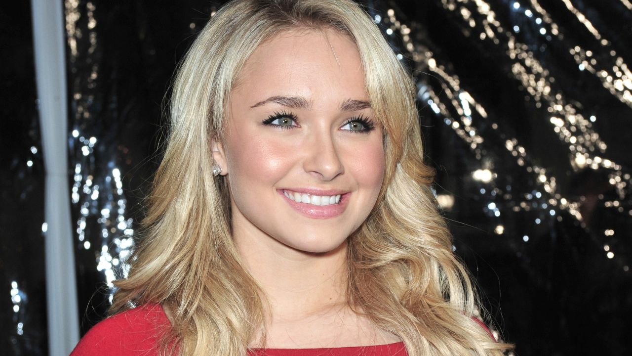 Portrait of a smiling blonde woman with long wavy hair wearing a red top against a dark, sparkling background in a close-up shot. (informative)