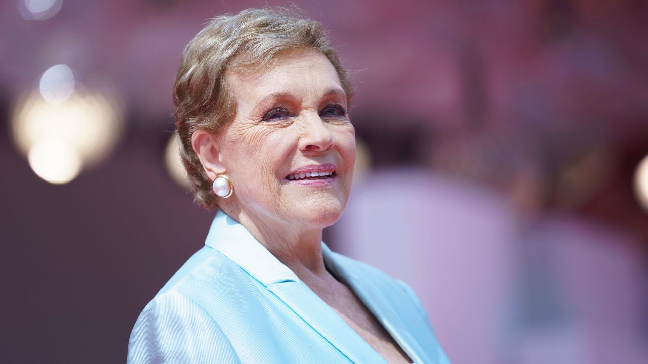 Smiling older woman with short blond hair in a light blue blazer and pearl earrings at a formal event.