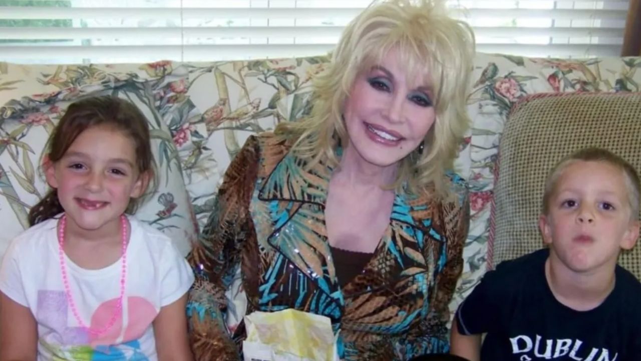 Smiling woman with blonde hair sitting between a girl and a boy on a floral couch.