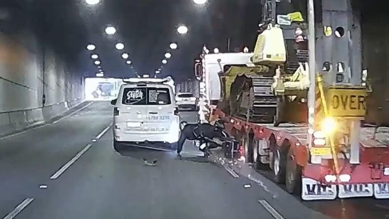 White van stopped in a tunnel beside a large tow truck; a person sits on the ground amid scattered debris behind the van and truck edge.