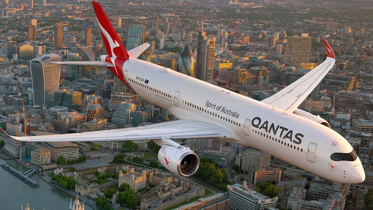 Qantas airliner labeled Spirit of Australia flying over a city skyline at sunset.