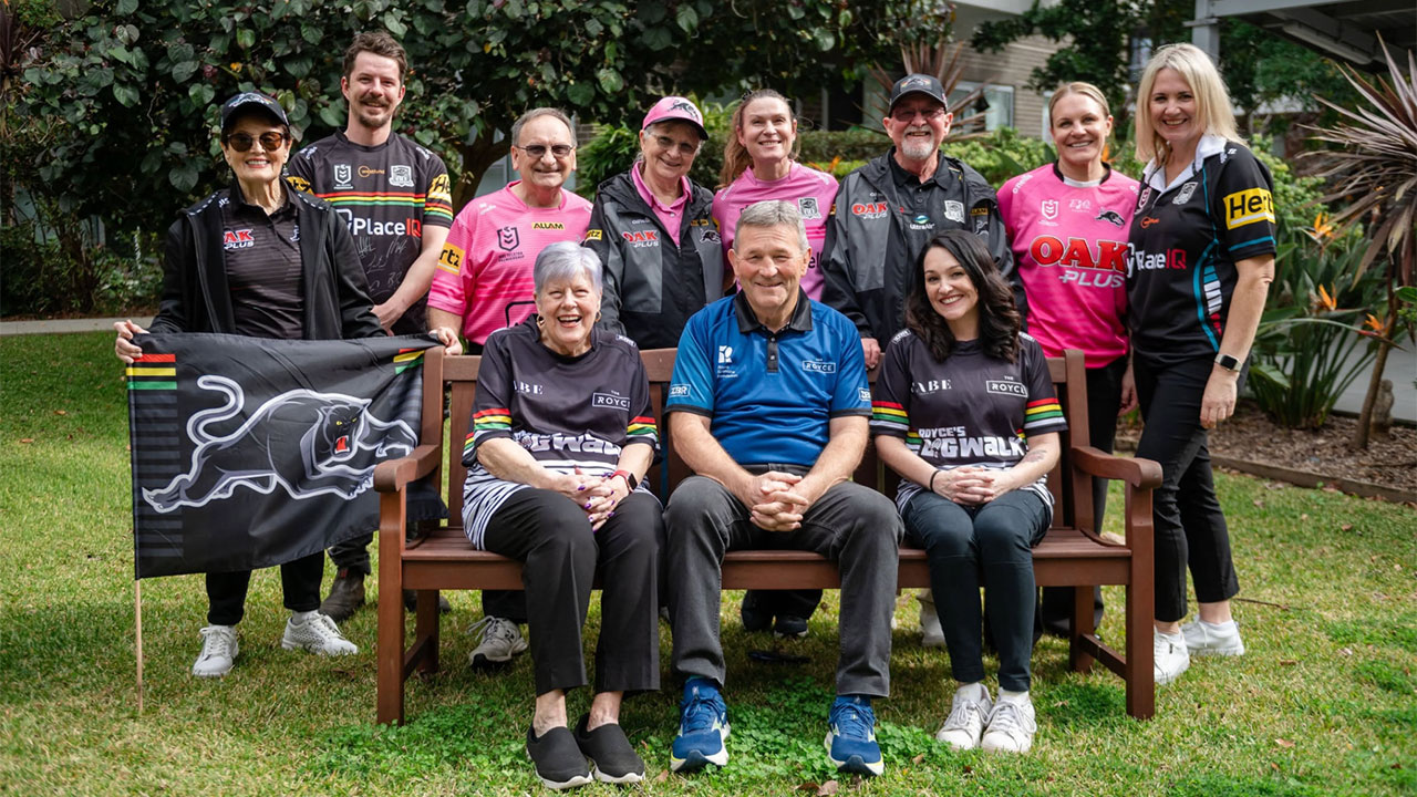Group of twelve people in team jerseys posing on and behind a wooden bench in a garden, smiling for a group photo.